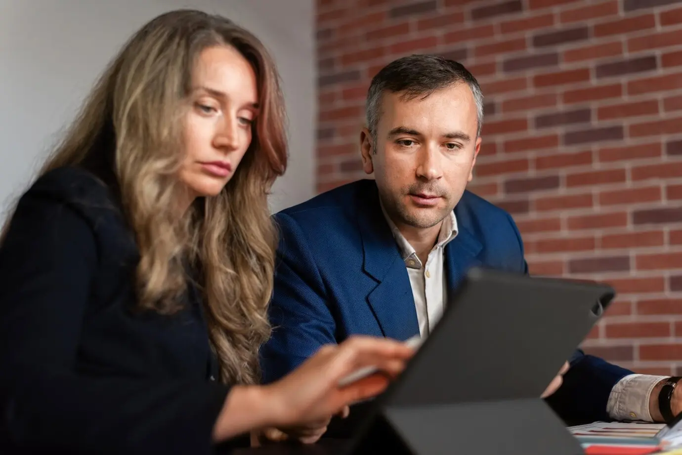 Деловая встреча в офисе: женщина и мужчина смотрят в планшет, на столе лежат бумаги и заметки.